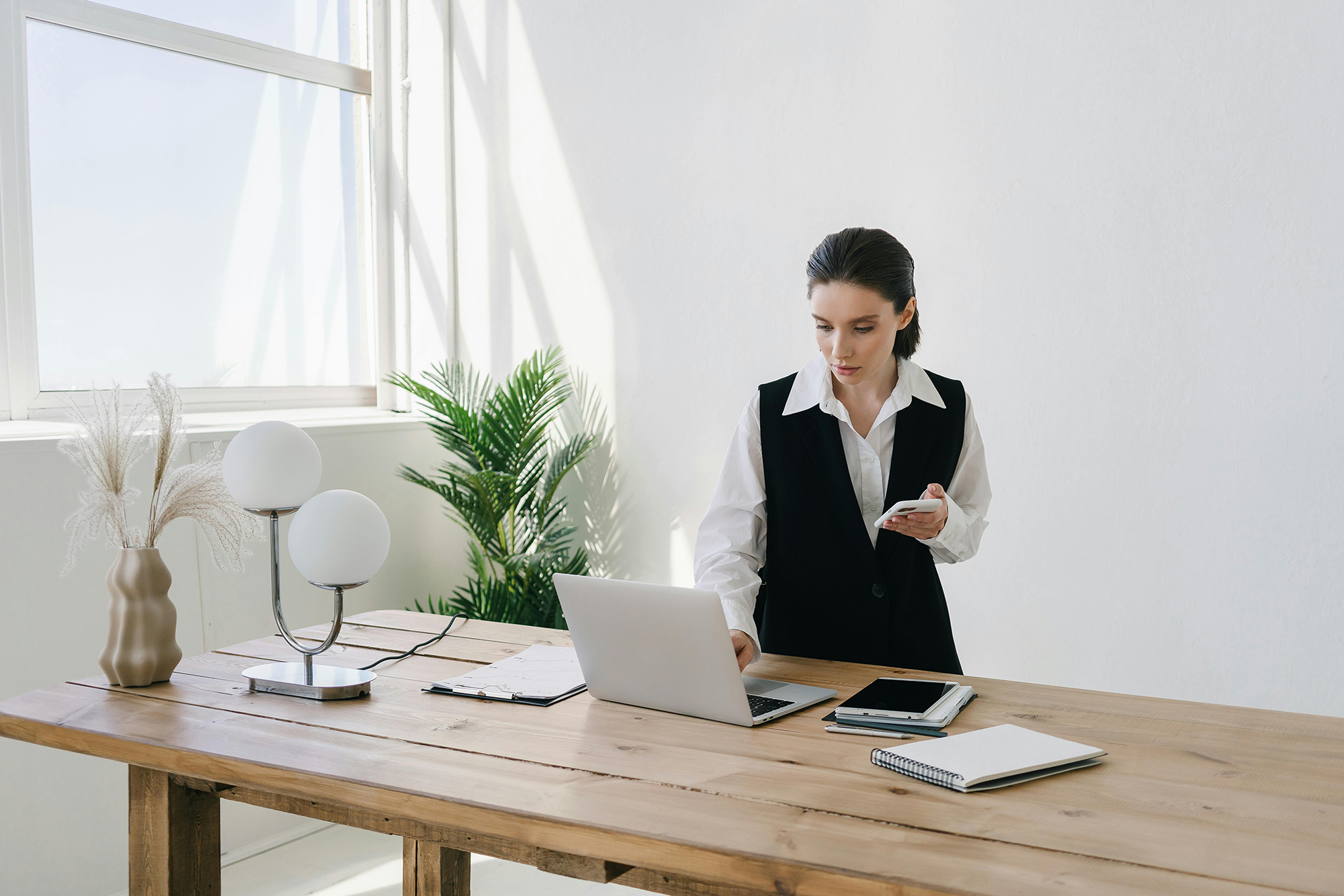 Frau mit Handy und Laptop bei Schreibtisch